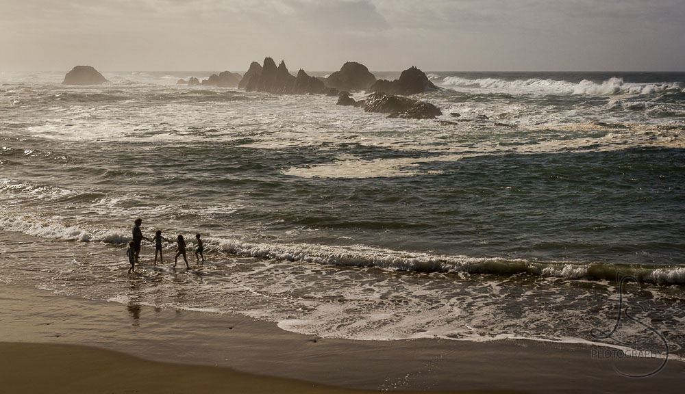 A family in silhouette, playing in the shallow waves near Newport, Oregon | LotsaSmiles Photography